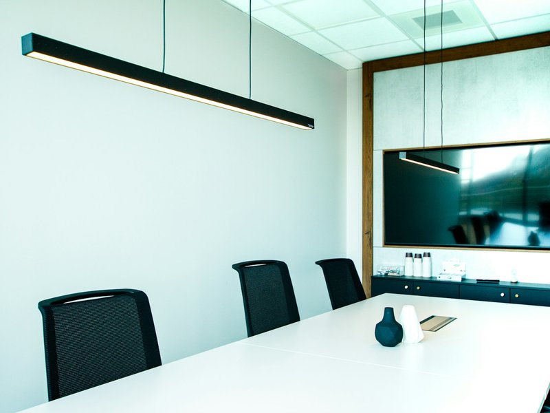 Meeting room with a white table, black chairs and a wall-mounted display