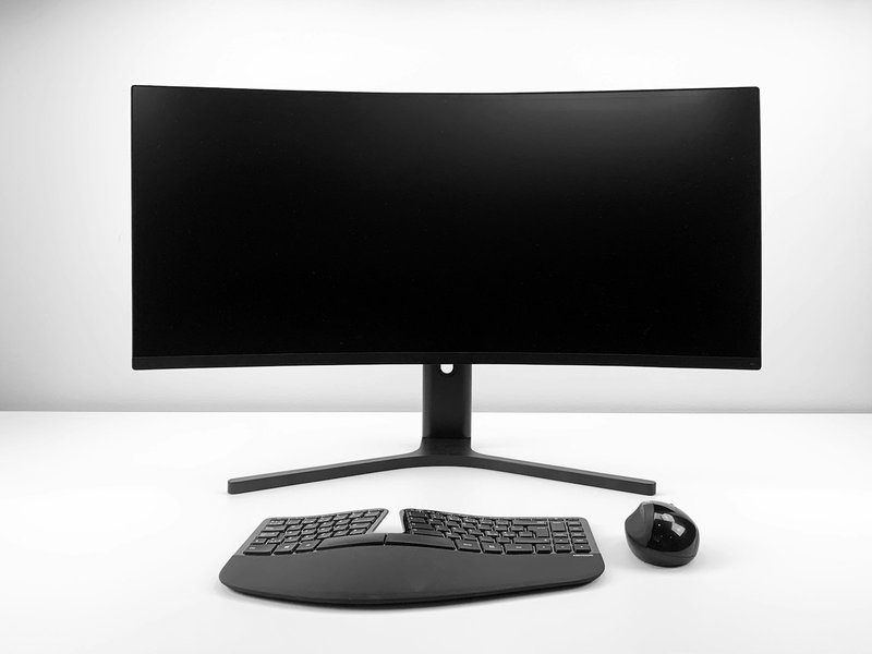 Curved black monitor with a keyboard and mouse on a white desk