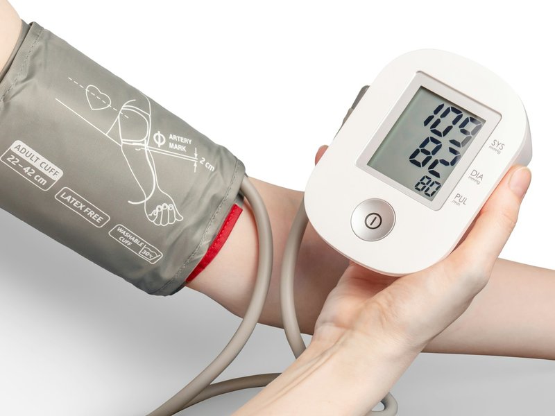 White digital blood pressure monitor beside a grey arm cuff