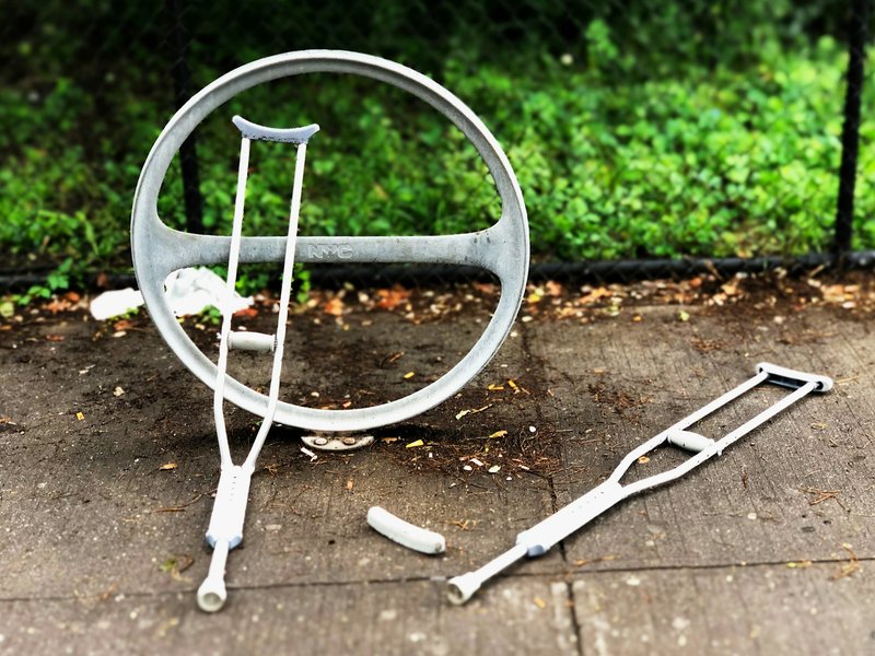 Pair of gray underarm crutches lying on a paved sidewalk