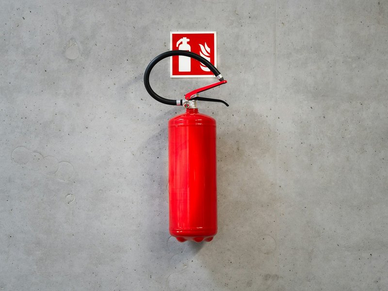 Red fire extinguisher mounted on a concrete wall below a fire sign