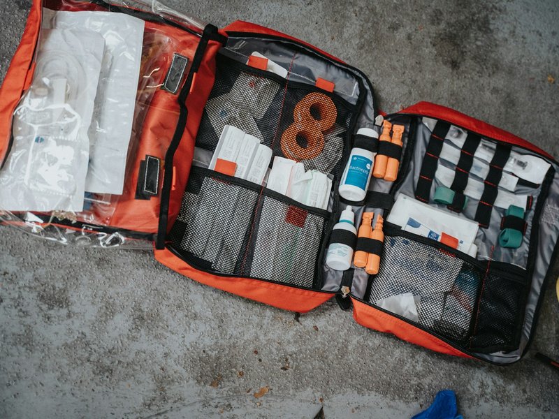 Open red first aid bag filled with bandages and supplies on concrete